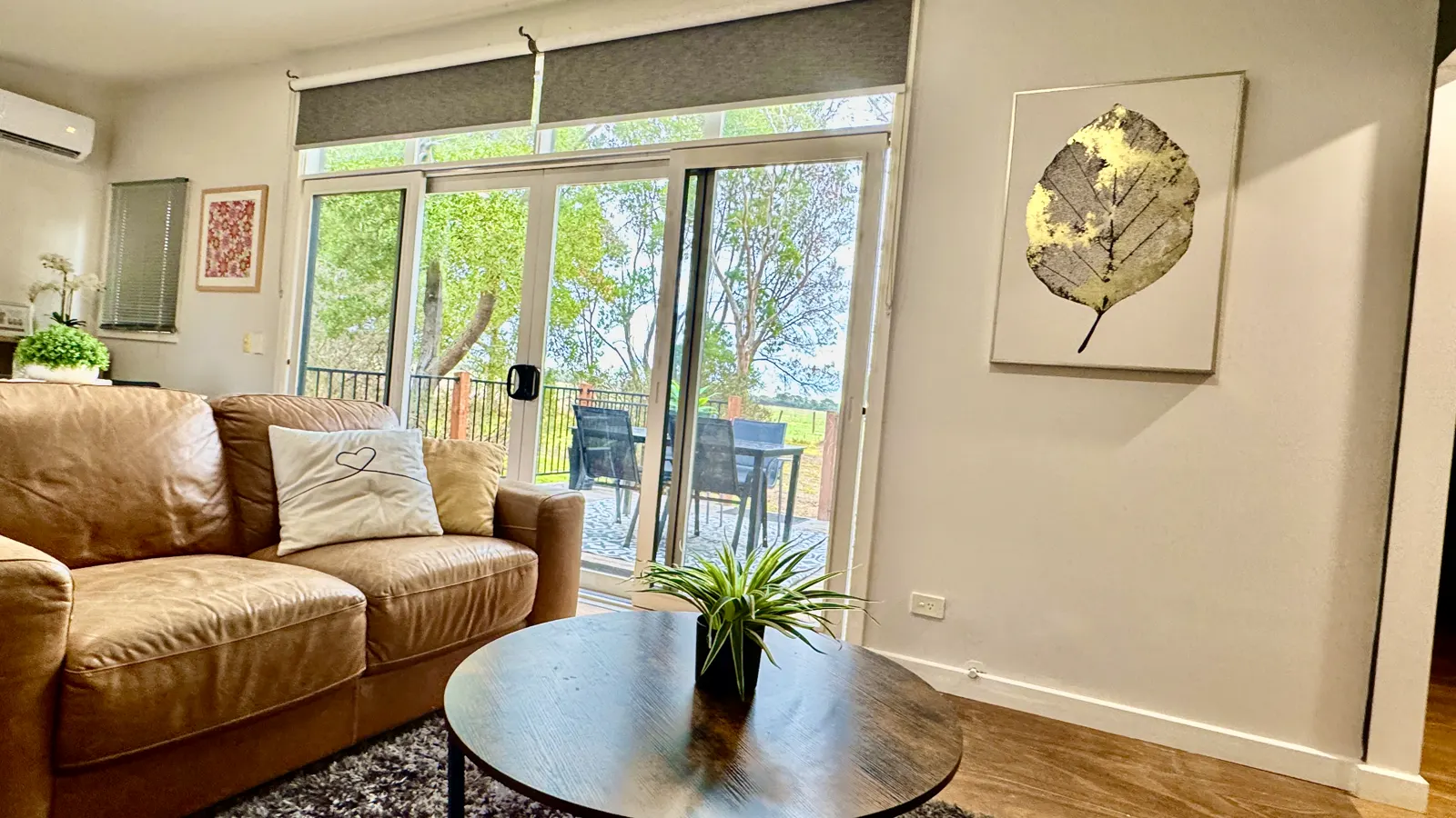 Living room with a tan sofa and sliding doors opening to the deck — Two-bedroom Villa 107, Cowes, Phillip Island