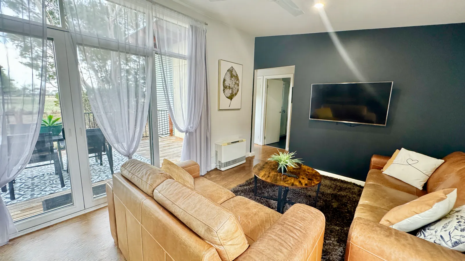 Living room with tan seating and a wall-mounted television beside the deck doors — Two-bedroom Villa 107, Cowes, Phillip Island