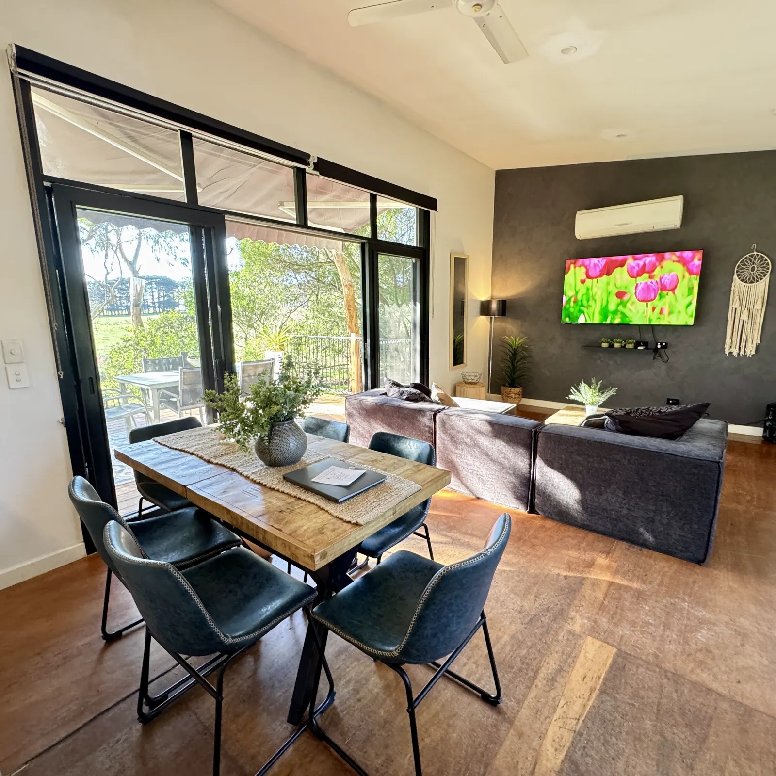 Open-plan living and dining room with timber floors and large deck-facing windows — Three-bedroom Villa 115, Cowes, Phillip Island