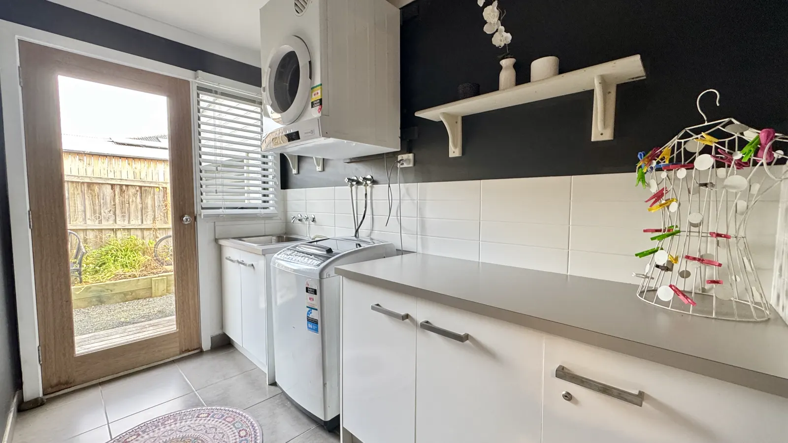 Laundry with a washing machine, sink and open door to the backyard — Coastal Tones holiday home, Cowes, Phillip Island