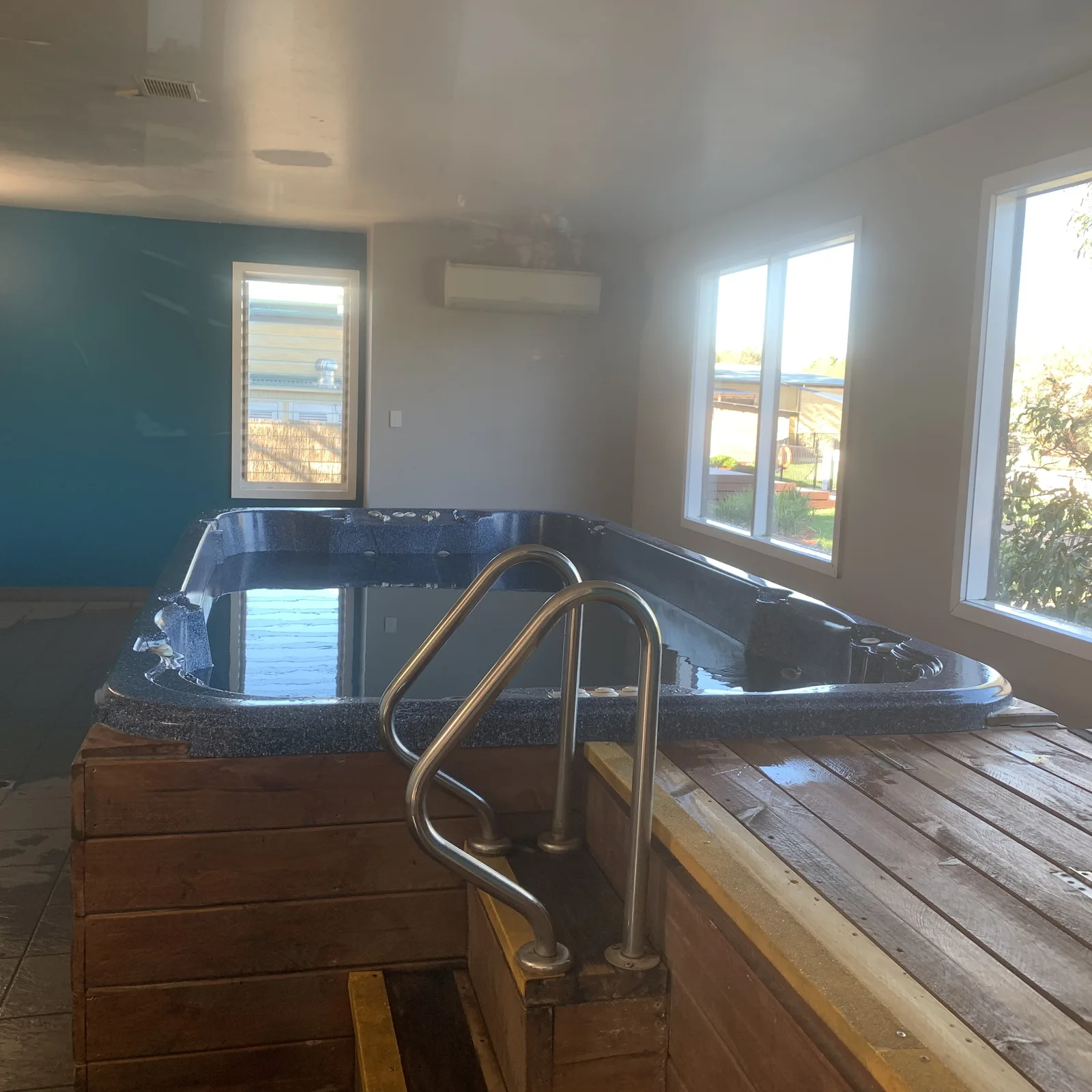 Indoor resort swim spa with steps, handrails and surrounding windows
