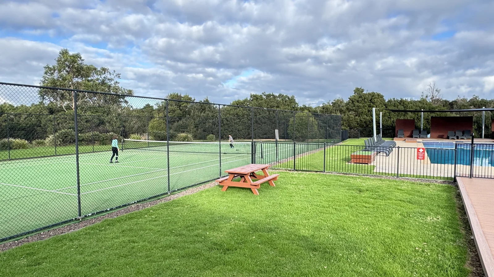 Guests playing tennis beside the resort pool and picnic area